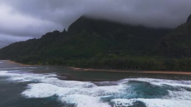 Hawaii, Kauai Adası 'ndaki Napali Sahili' nin havadan görünüşü, yemyeşil kayalıklar, sis, çarpan turkuaz dalgalar, altın kum ve bulutlu bir gökyüzü..