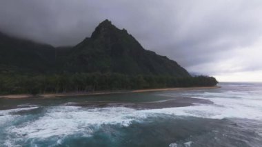 Kauai 'nin Napali uçurumlarının havadan görünüşü kıyıya vuran dalgalar, turkuaz okyanus, yoğun yeşillik ve alçak asılı bulutlar..