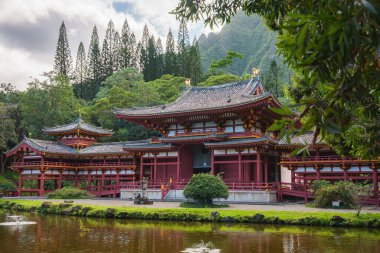 Hawaii, Oahu 'daki Byodo Tapınağı. Etrafı tropikal yapraklar, dingin bir gölet ve sisli dağlarla çevrili. Karmaşık mimari detaylar sergiliyor..