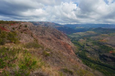 Hawaii, Kauai 'deki Waimea Kanyonu' nda kırmızı ve kahverengi uçurumlar, yeşil bir vadi ve bulutlu bir gökyüzünün altında dolambaçlı bir nehir bulunur..