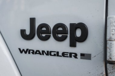 Beyaz bir Jeep Wrangler 'ın arka kısmının yakın görüntüsünde siyah Jeep ve Wrangler logoları stilize edilmiş Amerikan bayrağı tasarımı var. Toprak izleri görünür..