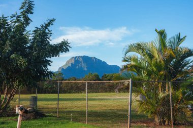 Kauai adasındaki Napali uçurumlarının engebeli dağı palmiye ağaçları ve yeşilliklerle çevrili. Zincirleme tel örgü ön planda çimenli bir alanı sarar.