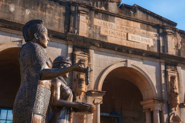 Historic Albert Spencer Wilcox Memorial Building in Kauai, Hawaii, with bronze statues in traditional Hawaiian attire and detailed stone facade. clipart