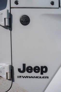 Trail Rated 4x4 rozeti, Jeep Wrangler logosu, kapı menteşesi ve off-road kullanımından kalma toprak izlerini gösteren beyaz Jeep Wrangler yan panelini kapatın..