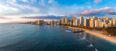 Gün batımında Honolulu, Oahu, Hawaii 'deki Waikiki Sahili' nin havadan görüntüsü. Turkuaz sular kumlu kıyılarla buluşur, yüksek katlı oteller ve arka planda bir rıhtım vardır..