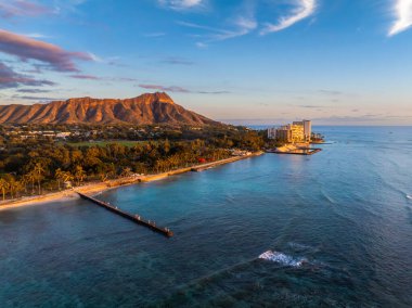 Hawaii, Oahu 'daki Waikiki Sahili' nin hava manzarası, günbatımında arkada Diamond Head Krateri, turkuaz sular, kumlu sahil şeridi ve sahil binaları..