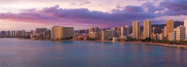 Gün batımında Honolulu, Oahu, Hawaii 'deki Waikiki Sahili' nin havadan görüntüsü. Yüksek binalar kıyı boyunca uzanır. Arka planda dağlar ve canlı gökyüzü vardır..