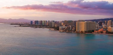 Waikiki Sahili 'nin, turkuaz suların, yüksek binaların ve gün batımında canlı bir gökyüzünün altındaki uzak dağların bulunduğu Honolulu, Hawaii' nin havadan görünüşü..