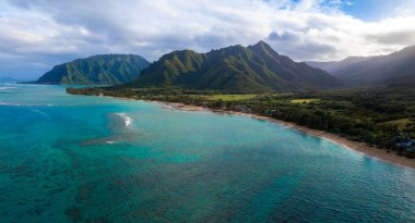 Hawaii, Oahu 'nun havadan görünüşü turkuaz suları, kumlu bir plaj ve dağınık bulutlu bir gökyüzünün altındaki yemyeşil Ko olau dağ sırasını gösteriyor..