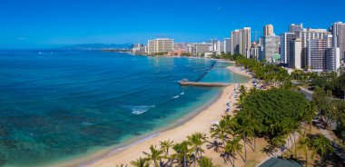 Turkuaz sular, Honolulu, Oahu 'da açık mavi gökyüzü altında, palmiye ağaçları, iskeleler ve yüksek binalarla Waikiki Sahili' nde kumlu kıyılarla buluşur..