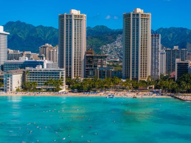 Aerial view of Waikiki Beach with turquoise waters, palm lined sandy shores, high rise buildings, and green mountains in Honolulu, Oahu, Hawaii. clipart