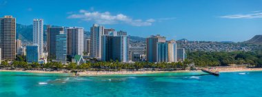 Turkuaz sular Waikiki Sahili 'nde kumlu kıyılarla buluşuyor, palmiye ağaçları ve yüksek binalarla kaplı, arka planda Diamond Head krateri var..