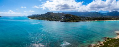 Hawaii, Oahu 'nun hava manzarası turkuaz suları, mercan resifleri, yeşil tepeler ve parçalı bulutlu bir gökyüzünün altındaki küçük bir kıyı kasabasını gösteriyor..