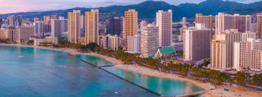 Gün batımında Honolulu, Oahu, Hawaii 'deki Waikiki Sahili' nin havadan görüntüsü. Turkuaz sular, kumlu kıyılar, palmiye ağaçları ve yüksek binalar görülebilir.
