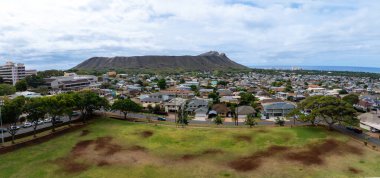 Panoramic aerial view of a residential area in Oahu, Hawaii, featuring Diamond Head Crater, a grassy park, houses, and the ocean on the horizon. clipart