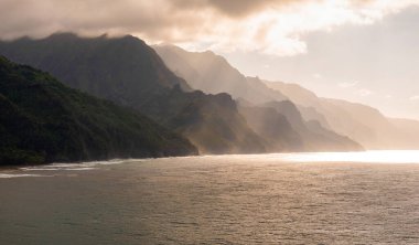 Hawaii 'deki Kauai Adası' ndaki Napali Sahili 'nin hava manzarasında engebeli uçurumlar, yemyeşil alanlar, sis, bulutlar ve okyanus üzerinde güneş ışığı var..