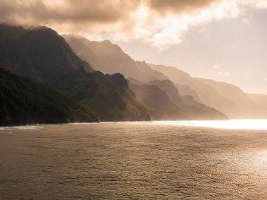 Hawaii, Kauai Adası 'ndaki Napali kıyısının engebeli kayalıkları Pasifik Okyanusu' na dökülüyor. Güneş ışığı yemyeşil ve tepeleri aydınlatıyor..