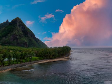 Kauai Adaları 'nın kıyı şeridinin havadan görünüşü, verimli Napali uçurumları, küçük bir sahil, yoğun bitki örtüsü ve pembe ve turuncu bulutlu canlı bir gökyüzü..