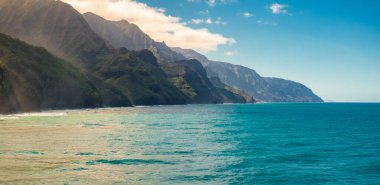 Kauai Adası 'ndaki Napali Sahili' nde turkuaz sulara inen engebeli yeşil uçurumlar var. Güneş ışığı dramatik manzarayı aydınlatıyor..