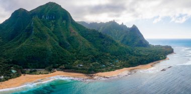 Kauais Napali uçurumları, altın kumlu plajlar, turkuaz sular ve kıyı şeridi yakınlarındaki dağınık yapılarla yoğun yeşillikler..