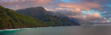 Kauai Adası 'ndaki Napali Sahili' nin yeşil tepeleri pembe ve turuncu bulutlarla dolu renkli gökyüzünün altında turkuaz sulara iniyor..