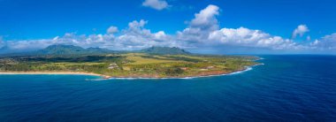 Mavi okyanus, kumlu sahil, yemyeşil yemyeşil, Napali uçurumları, yuvarlanan tepeler ve dağınık binaları gösteren Kauais kıyısı perspektifi..