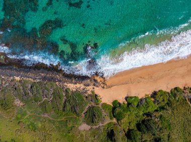 Turkuvaz suları, volkanik kayalar ve görünür sualtı oluşumları olan yemyeşil bitki örtüsüyle çevrili Kauai adasındaki altın kum plajı..