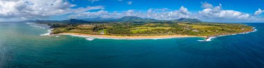 Hawaii 'deki Kauai Adası' nın havadan görünüşü, kumlu bir kumsal, turkuaz bir okyanus, yemyeşil bir manzara, dağınık binalar ve uzaktaki Napali uçurumlarını gösteriyor..