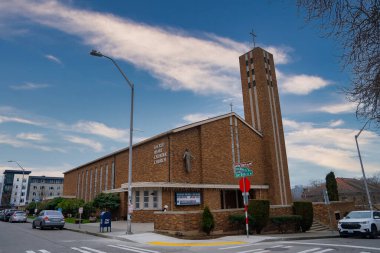 Kutsal Yürek Katolik Kilisesi, yüksek çan kulesi olan tuğla bir bina, ağaçlar ve şehir manzarası ile çevrili Doğu 6..