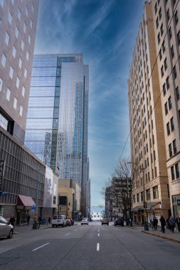 Seattle, ABD 'de modern ve klasik binalarla dolu işlek bir cadde. Camdan bir gökdelen gökyüzünü yansıtır ve su uzaktan görülebilir..
