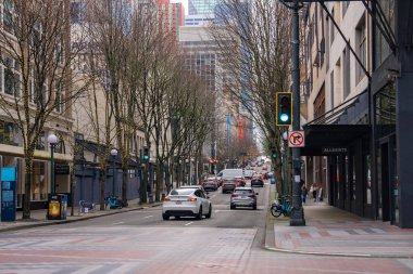 Seattle, ABD şehir merkezinde, yapraksız ağaçlar, çok katlı binalar, araçlar, yayalar ve serin bir sezonda yeşil trafik ışığı bulunan bir cadde..