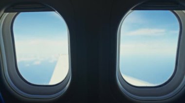 Kanadı, mavi gökyüzünü ve aşağıdaki uçsuz bucaksız okyanusu gösteren bir uçak penceresinden bak. Uçak durmaksızın hareket ediyor, sakin bir hava perspektifi sunuyor..
