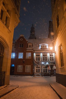 Rigas 'ın eski kasabasındaki kaldırım taşından caddelere kar yağıyor. Tarihi binalar, kilise kulesi, sıcak sokak lambası ve görünür süslemeleri var..
