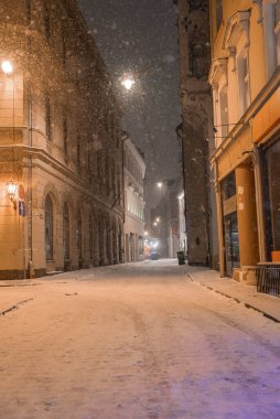 Karlı bir kış akşamında Rigas 'ın eski kasabasında, sıcak sokak lambalarıyla aydınlatılmış sessiz bir cadde. Süslü cepheli tarihi binalar cadde boyunca uzanır..