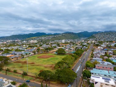 Hawaii, Oahu adasındaki yerleşim alanının havadan görüntüsü, arka planda beyzbol sahası, ana yol ve yemyeşil dağlar bulunan bir merkez parkı var..