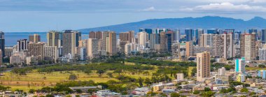 Modern yüksek binalar, yeşil bir park, Pasifik Okyanusu ve berrak gökyüzü altında uzak bir sıradağdan oluşan Honolulu, Hawaii 'nin hava manzarası..