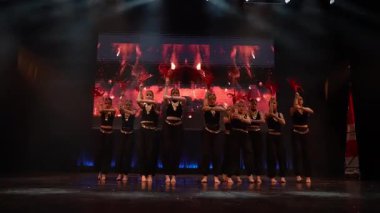 Siyah ve altın elbiseli çocuklar ateşli dijital arka plan, dramatik ışıklandırma ve kırmızı alev aksesuarlarıyla sahnede senkronize bir dans gerçekleştiriyorlar..