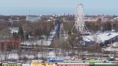 Güneşli bir kış gününde Riga 'nın hava manzarası, kar, dönme dolap, modern bir gökdelen, renkli trenler, hafif trafik ve yükselen baca dumanı..