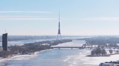 Güneşli bir kış gününde Riga 'nın havadan görünüşü, Daugava Nehri' nin sergilenmesi, karla kaplı manzaralar, Ulusal Kütüphane, ve şehir genelinde süpürme tepsisi..