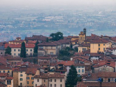 İtalya 'daki Bergamos eski kasabasının manzarası, kırmızı kiremitli çatılar, küçük bir çan kulesi, modern şehir ve kırsal kesimin puslu bir arka planı..