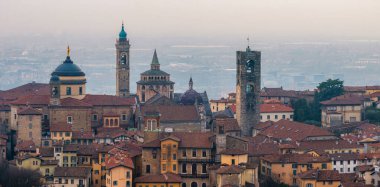 Bergamos 'un Santa Maria Maggiore Bazilikası, Campanone ve Cappella Colleoni' nin bulunduğu terasotta çatıları ve puslu bir günbatımı manzarası.