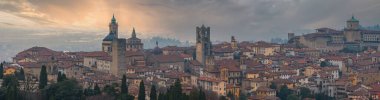 İtalya 'nın Bergamos şehrinin manzarasında Santa Maria Maggiore Bazilikası, Torre del Gombito, kırmızı kiremitli çatılar ve gün batımında yemyeşil alanlar yer almaktadır..