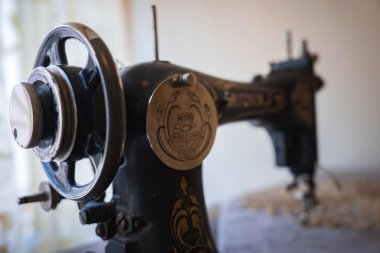 Karmaşık altın çiçek desenleri ve nilüfer amblemi ile iyi korunmuş eski bir dikiş makinesi. Yumuşak ışıklandırılmış arka plan ve bulanık perdeler..