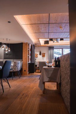 Ahşap zemin, açık ahşap tavan panelleri, modern kolye ışıkları, döşenmiş sandalyeler ve açık hava manzaralı büyük pencerelerin bulunduğu otel yemek salonu..