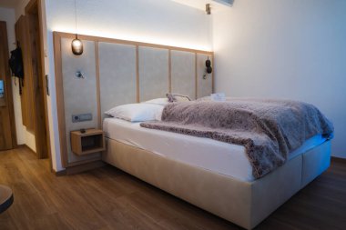 Ischgl, Avusturya 'da, tüylü, yastıklı yatak başlığı, ahşap döşeme, kolye ışığı ve minimalist dekorun yer aldığı rahat bir otel odası..