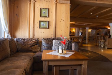 Sıcak ahşap panelli rahat bir dinlenme odası, rahat bölmeli kanepe, desenli yastıklar, yüksek tabureli bir bar alanı, ve içeri akan doğal ışık..