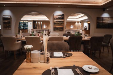 Yemek salonunda ahşap masalar, peluş sandalyeler, beyaz çiçekler, çerçeveli sanat eserleri, aralıklı aydınlatma, kemerli açıklıklar ve bir şarap sergisi yer alıyor..