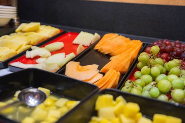 Kapalı büfe, dilimlenmiş ananas, kavun, kavun ve tepside üzüm. Koyu bir tezgahta ve ahşap panellerde doğranmış meyveli siyah tepsi..