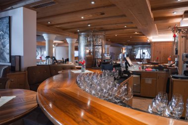 Şarap kadehleriyle cilalanmış ahşap tezgah, sıcak ahşap tavan, beyaz sütunlar, hafif ışıklandırma ve Avusturya, Ischgl 'de modern bar ekipmanları..