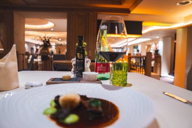 Sıcak, zarif bir restoranda ahşap aksanlı ve modern dekorlu bir masada kırmızı şarap, maden suyu ve zeytinyağı bulunan bir gurme tabağı..